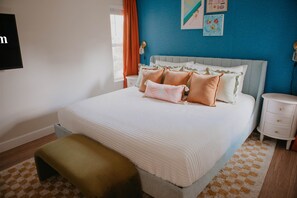 Ein Schlafzimmer mit einem Bett, Kissen, einem Nachttisch, einer Bank und einer Wand mit Kunstwerken.