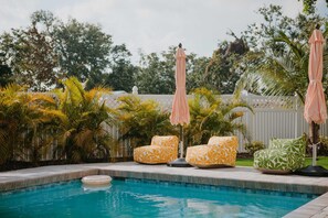 A swimming pool with lounge chairs and umbrellas, surrounded by palm trees and a white fence. - Sleeps 20 Games Basketball Pool Movie Room (Bradenton)