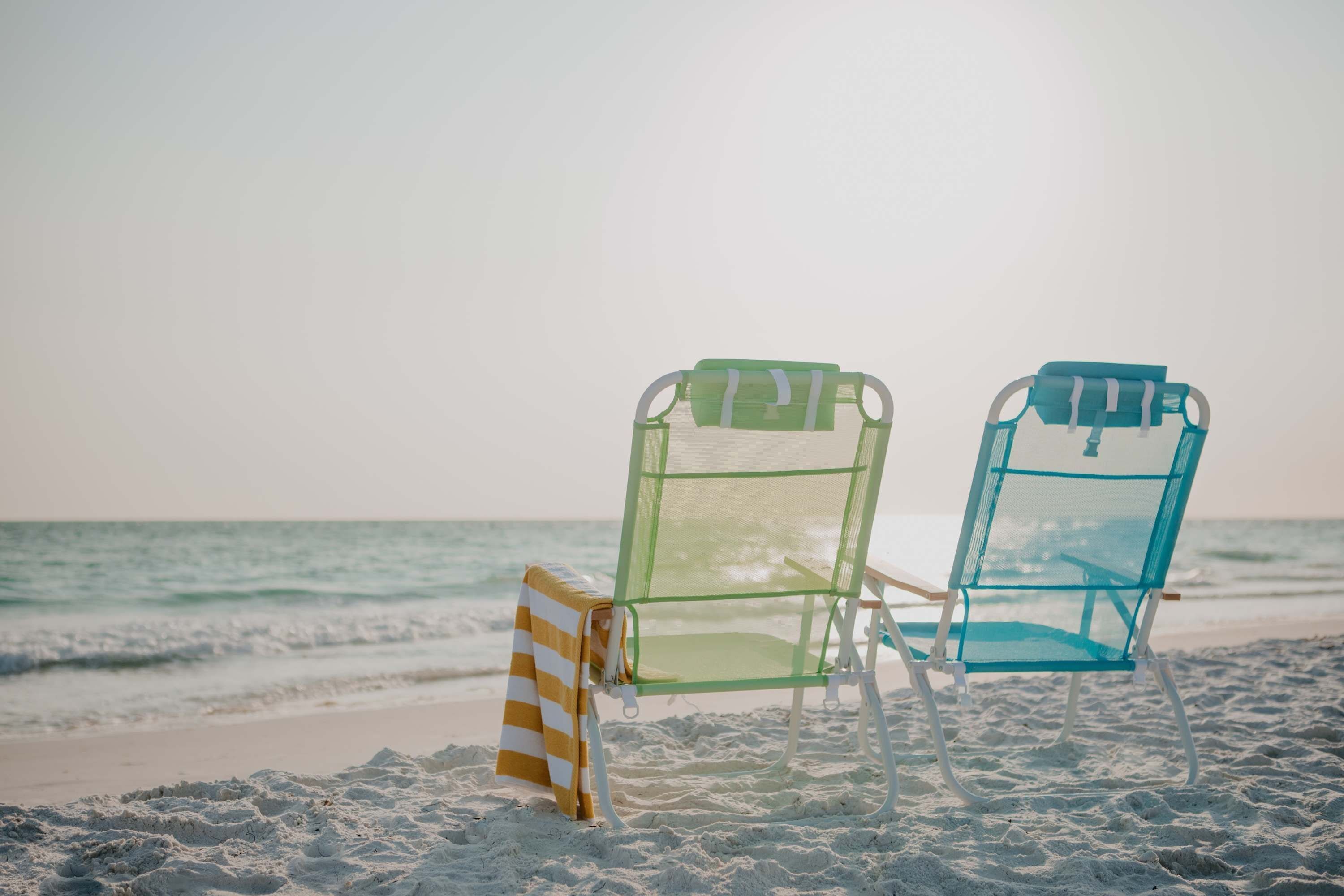 Two beach chairs with towels on a sandy beach by the ocean.