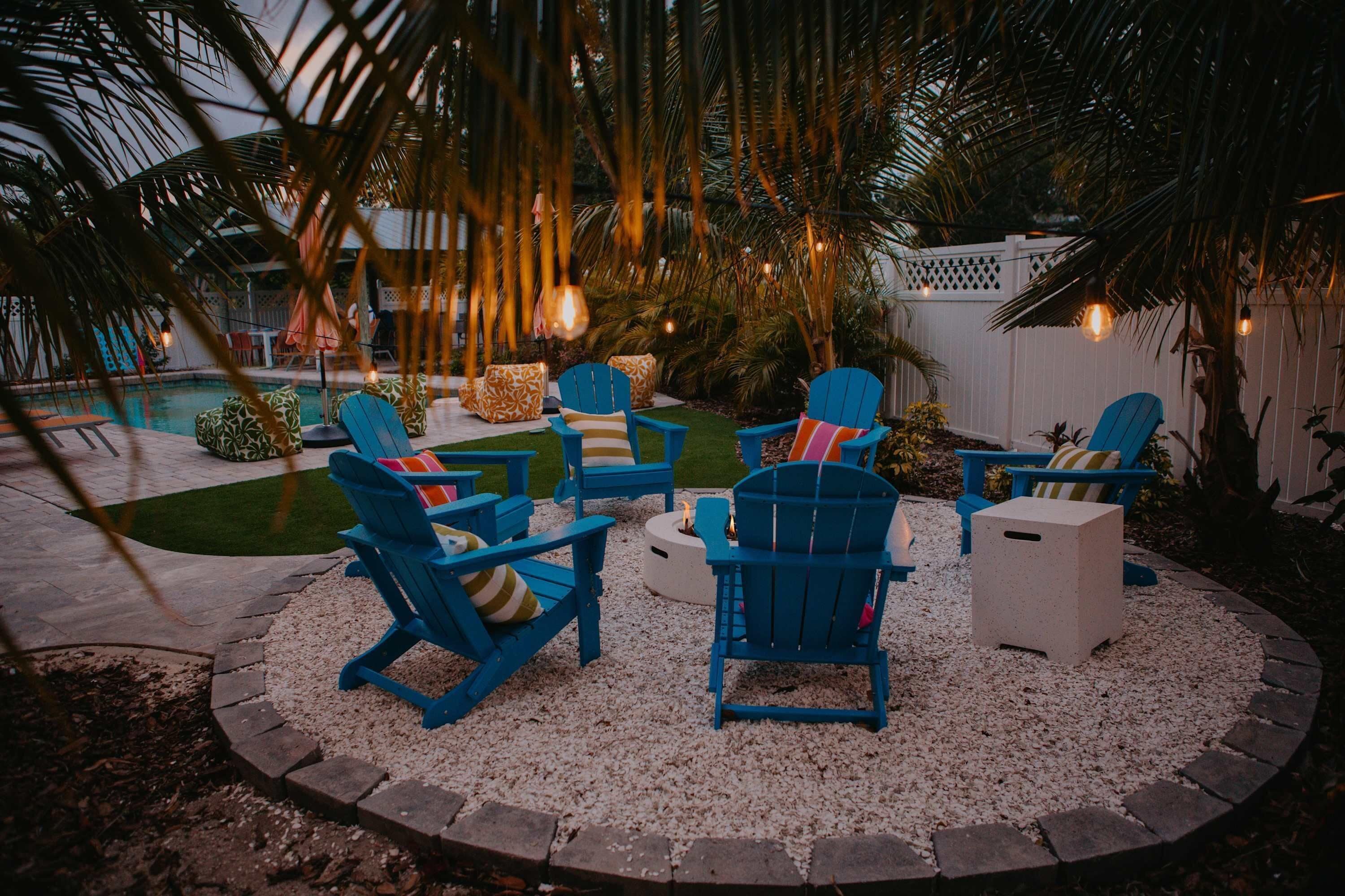 An outdoor seating area with blue Adirondack chairs and a small table, surrounded by a gravel circle.