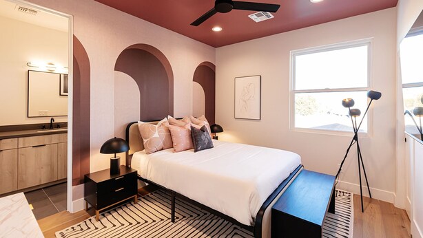 Ein Schlafzimmer mit Bett, Nachttischen, Deckenventilator, Fenster und Stehlampe.
