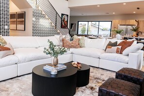 Ein modernes Wohnzimmer mit einem Ecksofa, einem Couchtisch und einer Treppe mit einem gemusterten Wandbild.