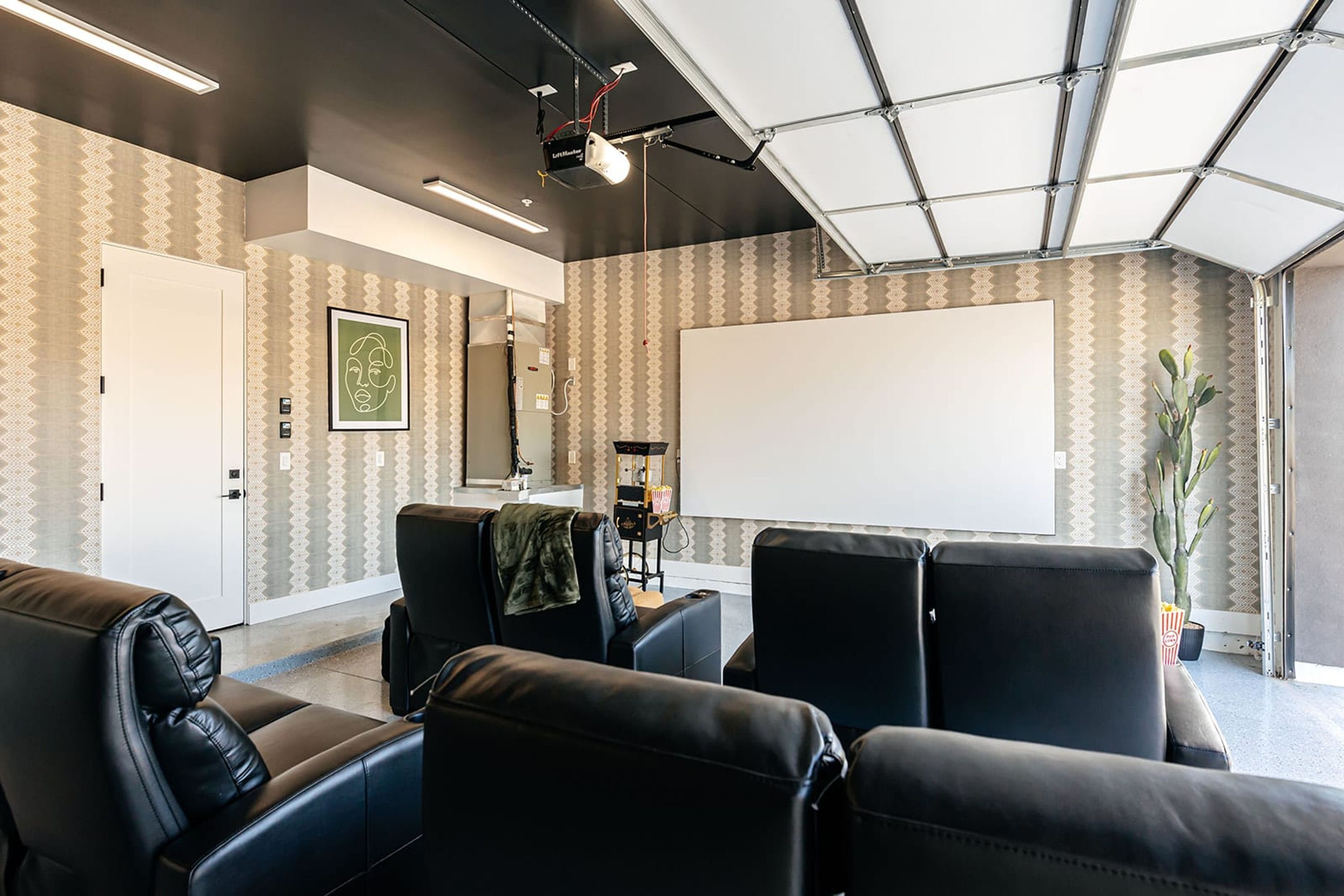 Una habitación con una gran pantalla blanca proyectora, asientos de cuero negro y un papel tapiz estampado.