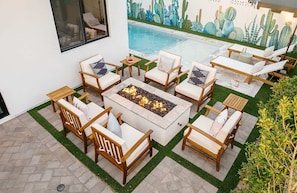 Ein Sitzbereich am Pool mit Feuerstelle, umgeben von Liegestühlen und einer Kakteen-Wandmalerei.