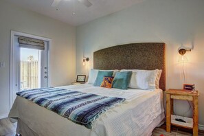 A bedroom with a bed, a nightstand, a wall-mounted lamp, and a door with a view of the outside. - Borracho Beach- Waterslide Pet Friendly (Port Aransas)