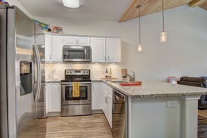 A modern kitchen with stainless steel appliances, white cabinetry, and a granite countertop. - Borracho Beach- Waterslide Pet Friendly (Port Aransas)