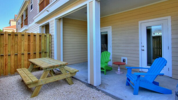 Eine überdachte Terrasse mit Holztisch und Stühlen, ein kleiner Tisch mit roter Oberfläche und ein grüner Stuhl.