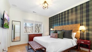 Una camera da letto con un letto, una panca, una cassettiera, uno specchio, una finestra e un muro a motivi tartan.