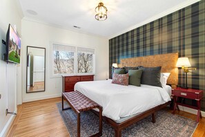 A bedroom with a bed, a bench, a dresser, a mirror, a window, and a plaid-patterned wall. - 7k Sqft Estate - Epic Amenities Fun - Sleeps 20 (Asheville)