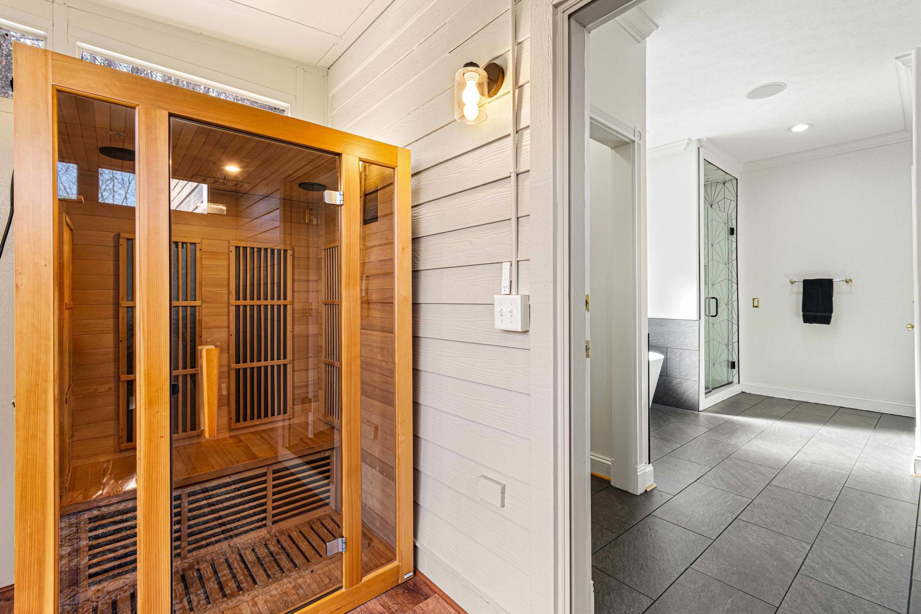 Una sauna de madera con puerta de vidrio, una lámpara en la pared y piso de baldosas.