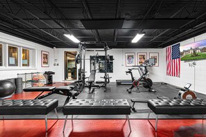 A gym with various exercise equipment, a bench press, a treadmill, and an American flag. - 7k Sqft Estate - Epic Amenities Fun - Sleeps 20 (Asheville)