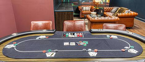 A casino table with poker chips and cards, leather chairs, and a sofa in the background.