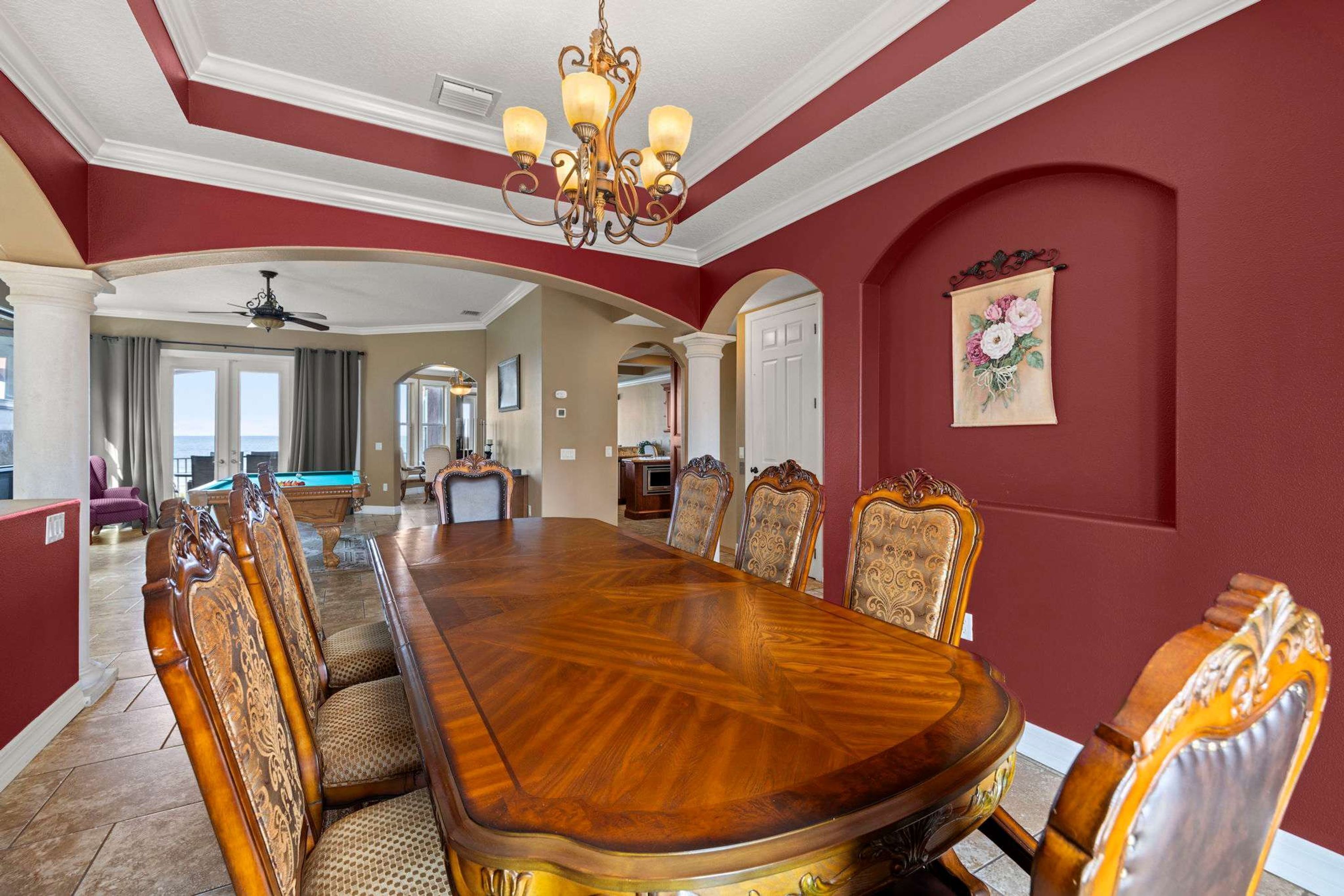 A dining room with a large wooden table and ornate chairs, a chandelier, and a view of the living area.