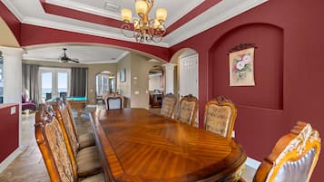Comedor con una gran mesa de madera y sillas ornamentadas, un candelabro y vista al área de estar.