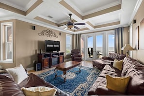 A spacious living room with a ceiling fan, a television, a fireplace, and a large window with a view. - Beachfront Villa Heated Pool Spa Pool Table (Treasure Island)