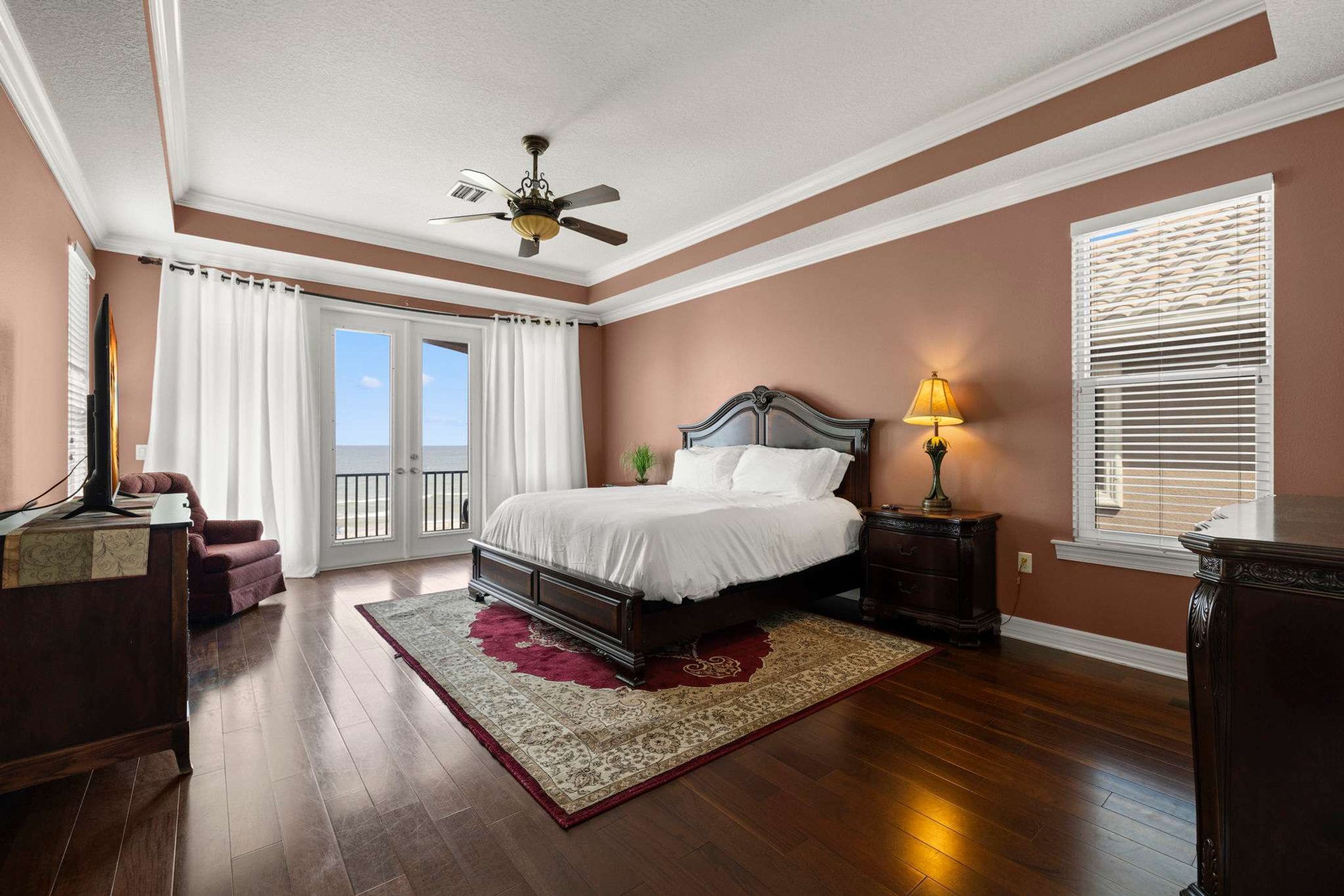 A bedroom with a bed, a nightstand, a lamp, a ceiling fan, and a view of the outdoors through a door.