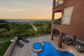 Ein Poolbereich mit Blick auf den Ozean, Gartenmöbel und ein Gebäude mit Balkon.