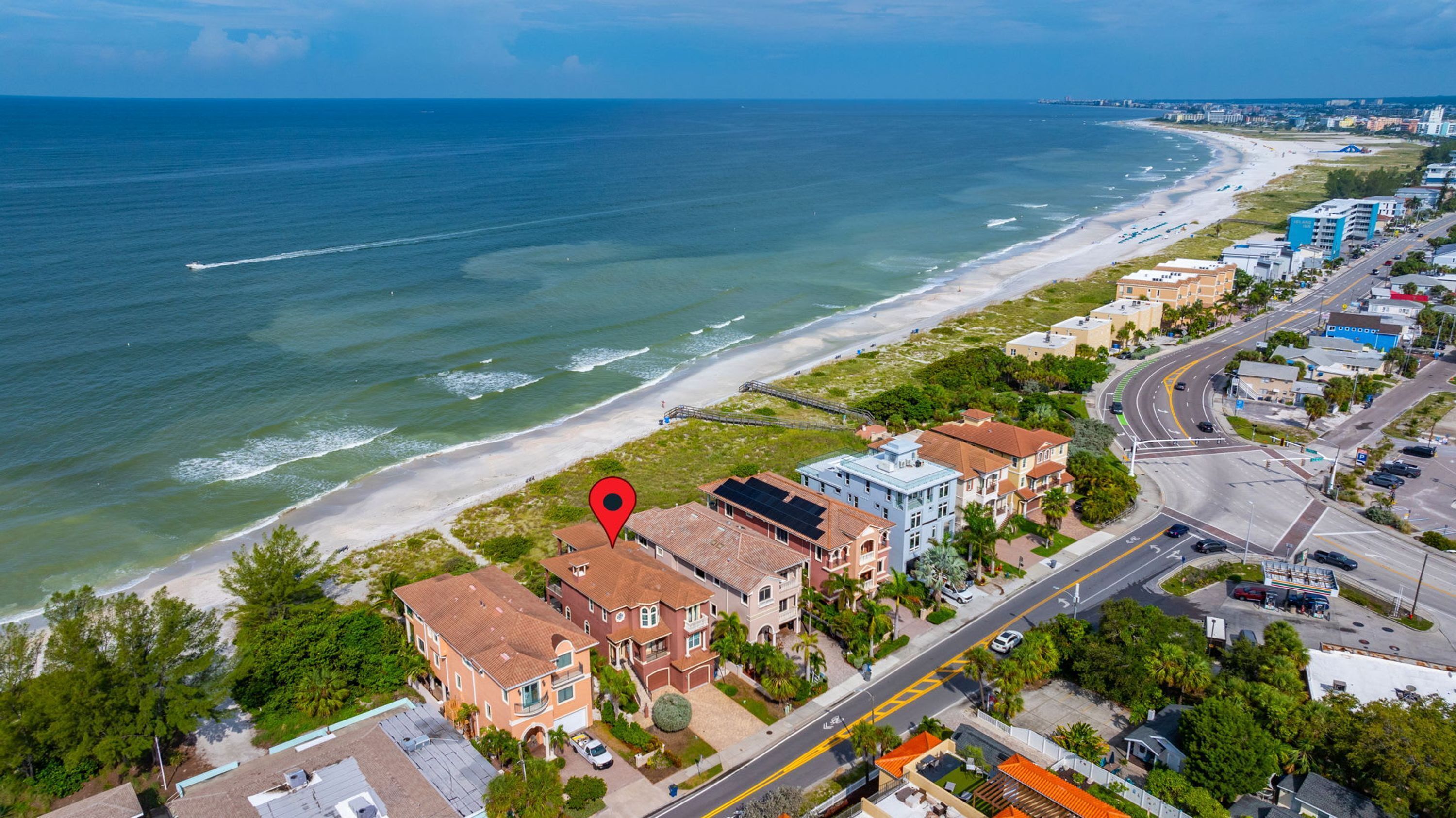 An aerial view of a coastal residential area with a beachfront, roads, and buildings.