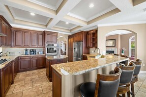 Eine geräumige Küche mit Granit Arbeitsplatten, dunklen Holzschränken, Edelstahlgeräten und einer zentralen Kochinsel mit Barhocker.