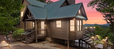 A two-story cabin with a stone foundation, a metal roof, and a deck with railings.