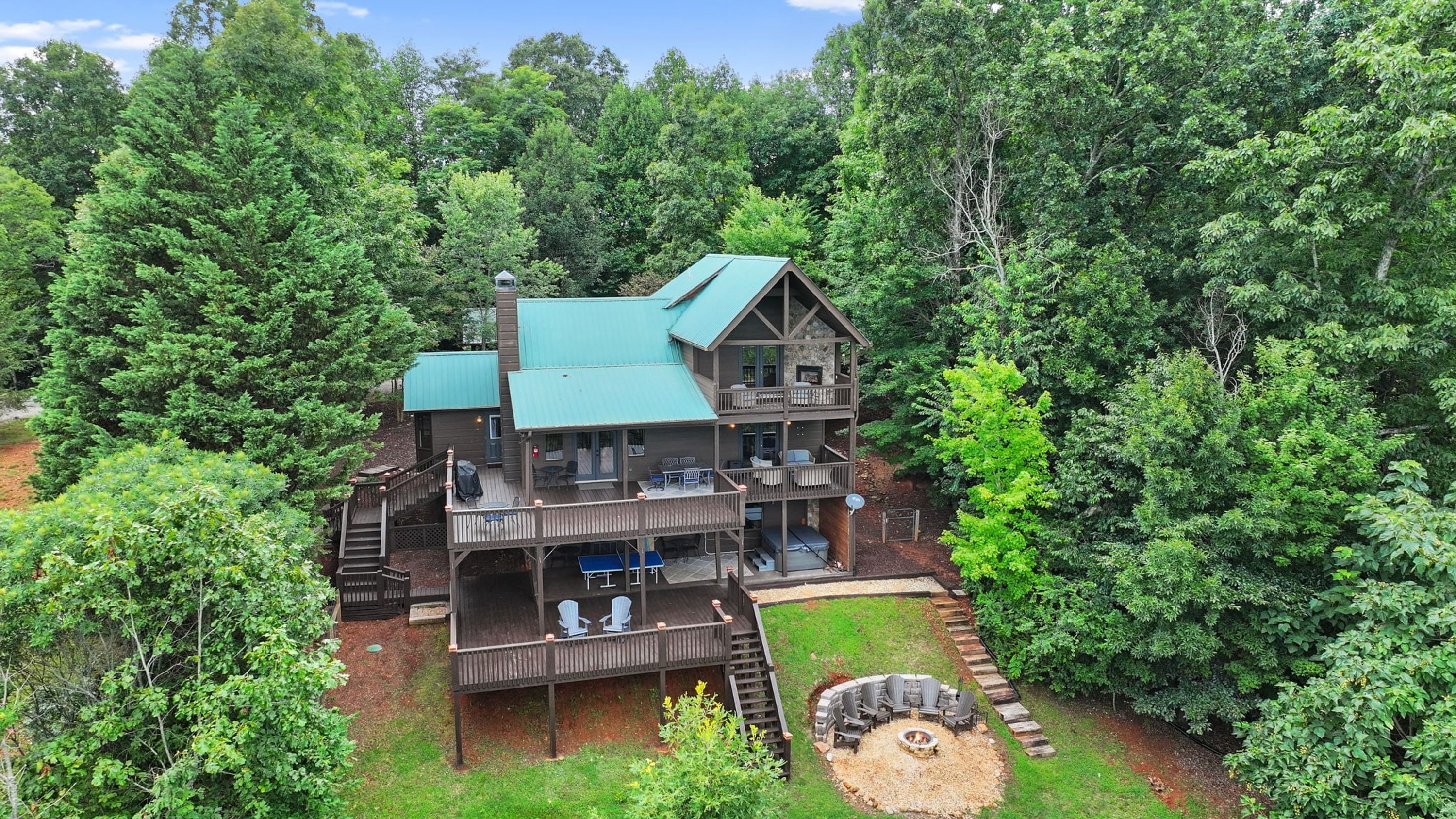 Eine mehrstöckige Hütte mit einer Terrasse und Sitzgelegenheit im Freien, umgeben von dichtem Wald.