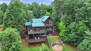Un chalet à plusieurs étages doté d’une terrasse et d’un espace salon extérieur, entouré d’une forêt dense.