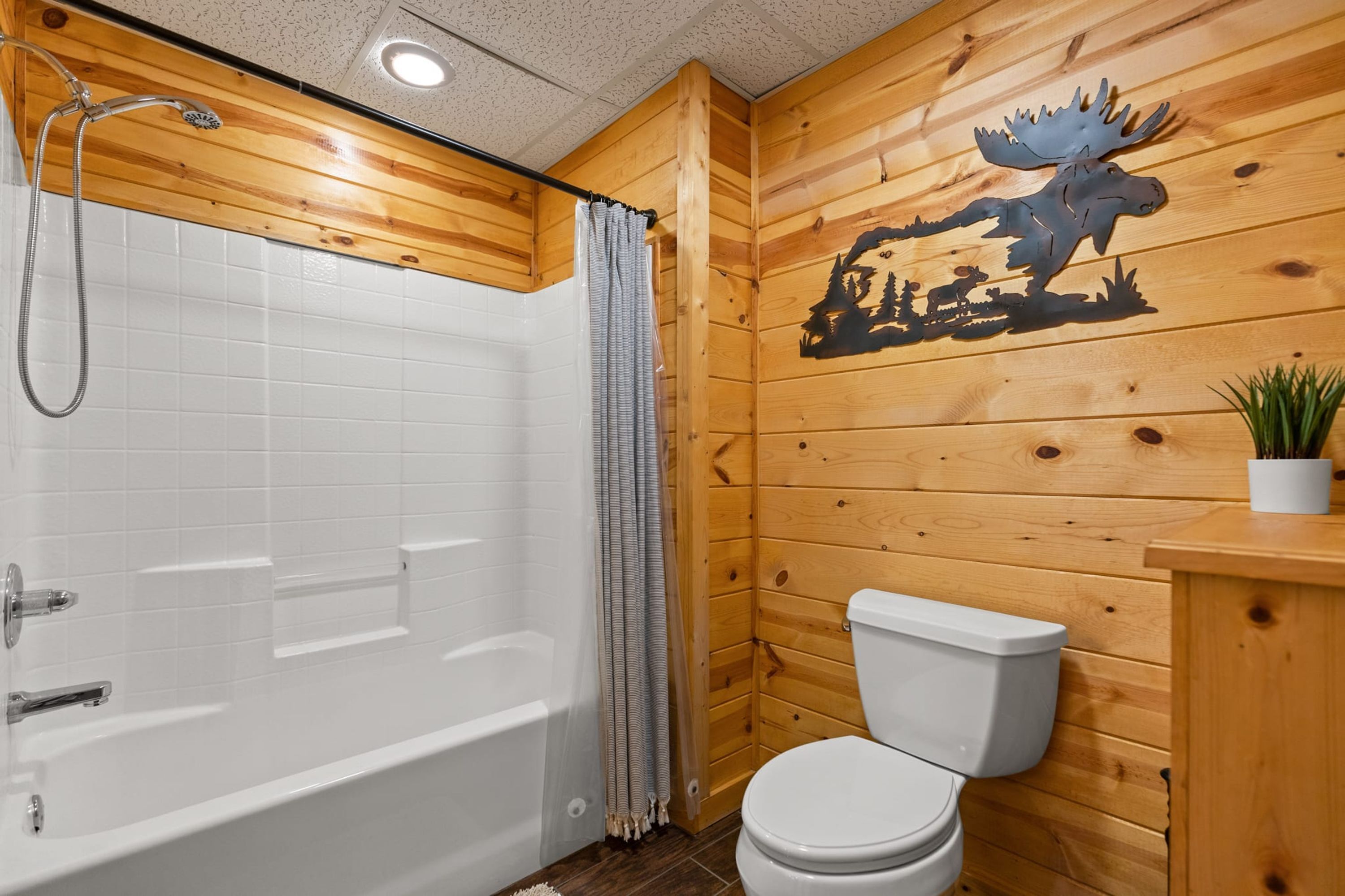 A wooden cabin bathroom with a bathtub, toilet, and a decorative wall featuring a moose.