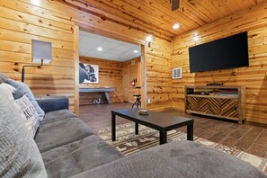 Ein gemütliches Blockhaus-Interieur mit einer Couch, einem Couchtisch, einem Flachbildfernseher und einem Kamin.