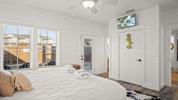 A bedroom with a bed, a ceiling fan, a TV, and a door with a view of the outside.
