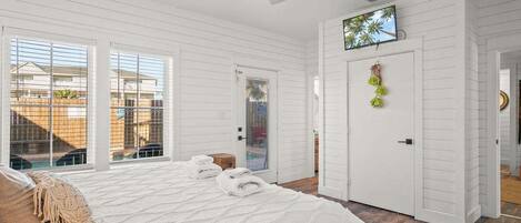 Un dormitorio con cama, ventilador de techo, televisión y puerta con vista al exterior.