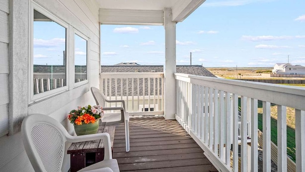 Ein überdachter Balkon mit Blick auf den Strand und ein entferntes Gebäude.