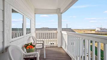 A covered porch with a view of the beach and a distant building.