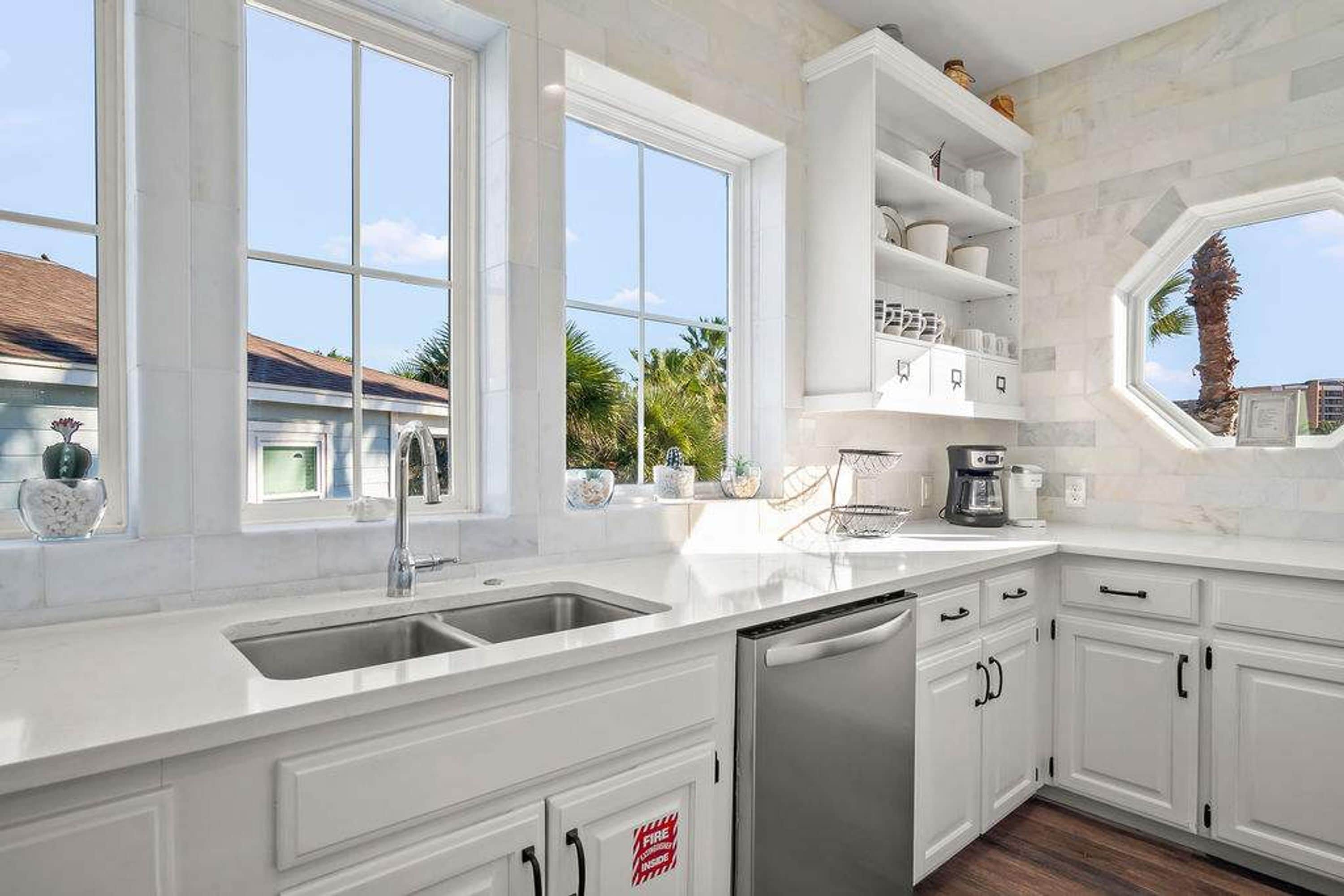 A modern kitchen with white cabinetry, a stainless steel sink, and a coffee maker.