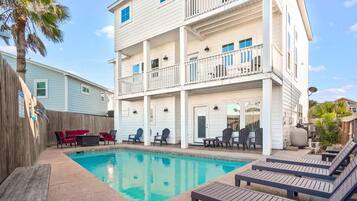 A multi-story building with a swimming pool, outdoor seating, and a wooden deck.
