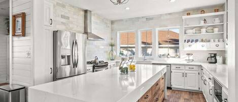 A modern kitchen with a large island, stainless steel appliances, and a view to the outside.
