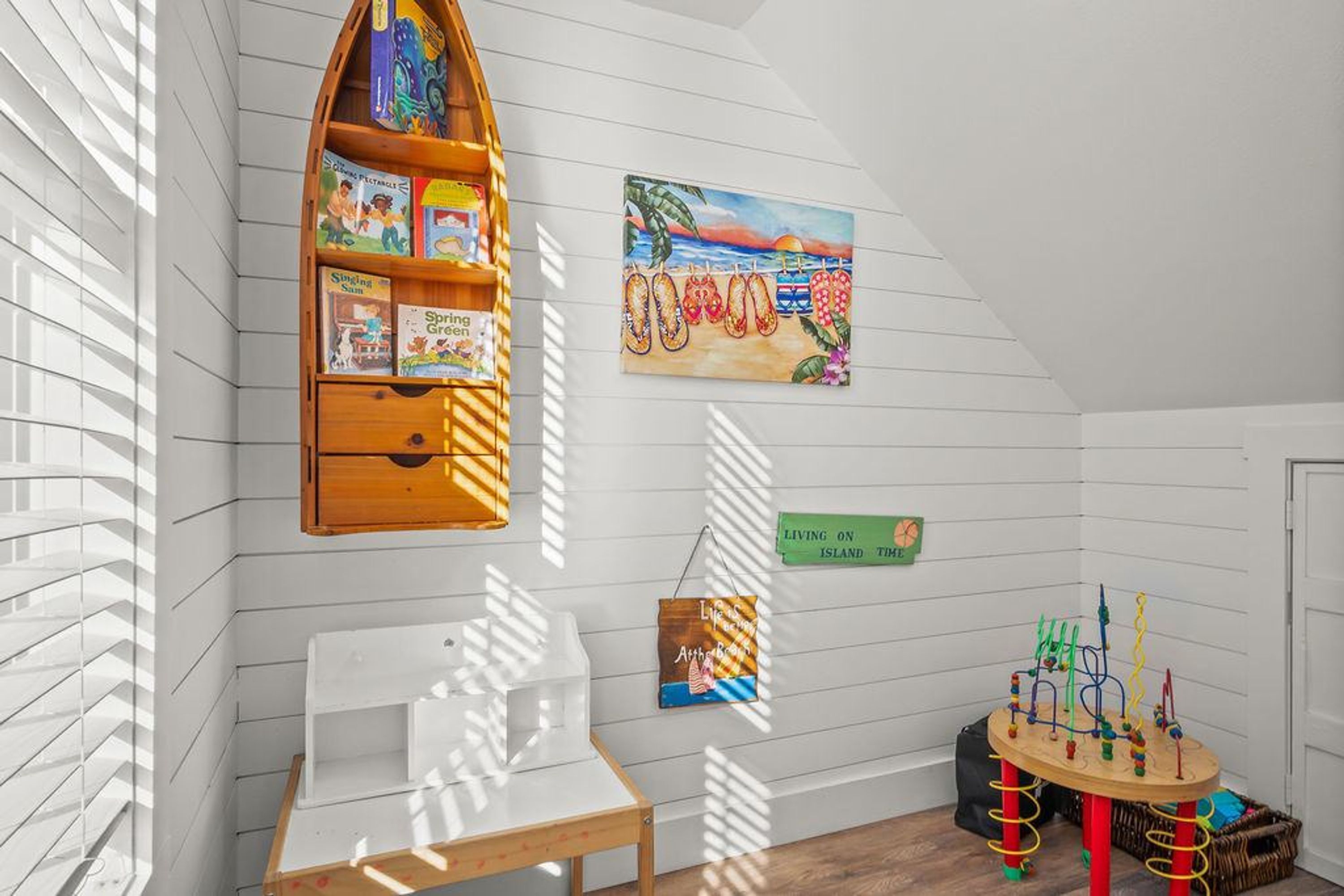 Habitació infantil amb una prestatgeria, un quadre, un cartell i una taula de jocs.