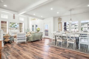 Un salon spacieux avec un grand canapé, un coin repas avec une table et des chaises blanches, et une cuisine à l’arrière-plan.