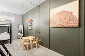 Une pièce avec un lit superposé, une table ronde avec des chaises, un luminaire suspendu et un grand tableau abstrait accroché au mur.