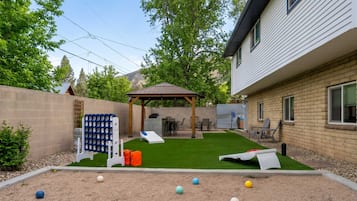 Un pati amb gespa artificial, zona de barbacoa i espai de seients cobert.