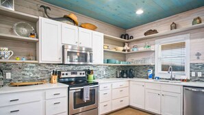 A modern kitchen with white cabinetry, a stainless steel oven, and a built-in microwave. - Sea Gypsy Fire Pit Community Pool Corn Hole (Port Aransas)