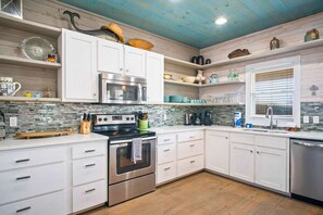 A modern kitchen with white cabinetry, a stainless steel oven, and a built-in microwave. - Sea Gypsy Fire Pit Community Pool Corn Hole (Port Aransas)