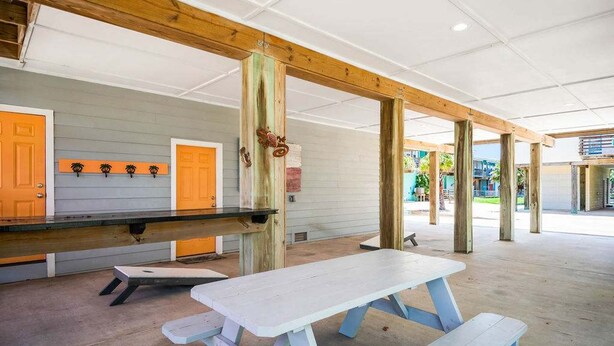 An outdoor covered picnic area with picnic tables and benches, wooden pillars, and doors. - Sea Gypsy Fire Pit Community Pool Corn Hole (Port Aransas)