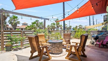An outdoor patio with wooden chairs and a round table, surrounded by a wooden fence and palm trees.