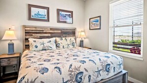 A bedroom with a bed, two nightstands, a wooden headboard, and three framed pictures on the wall. - Sea Gypsy Fire Pit Community Pool Corn Hole (Port Aransas)