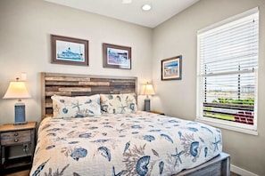 A bedroom with a bed, two nightstands, a wooden headboard, and three framed pictures on the wall. - Sea Gypsy Fire Pit Community Pool Corn Hole (Port Aransas)