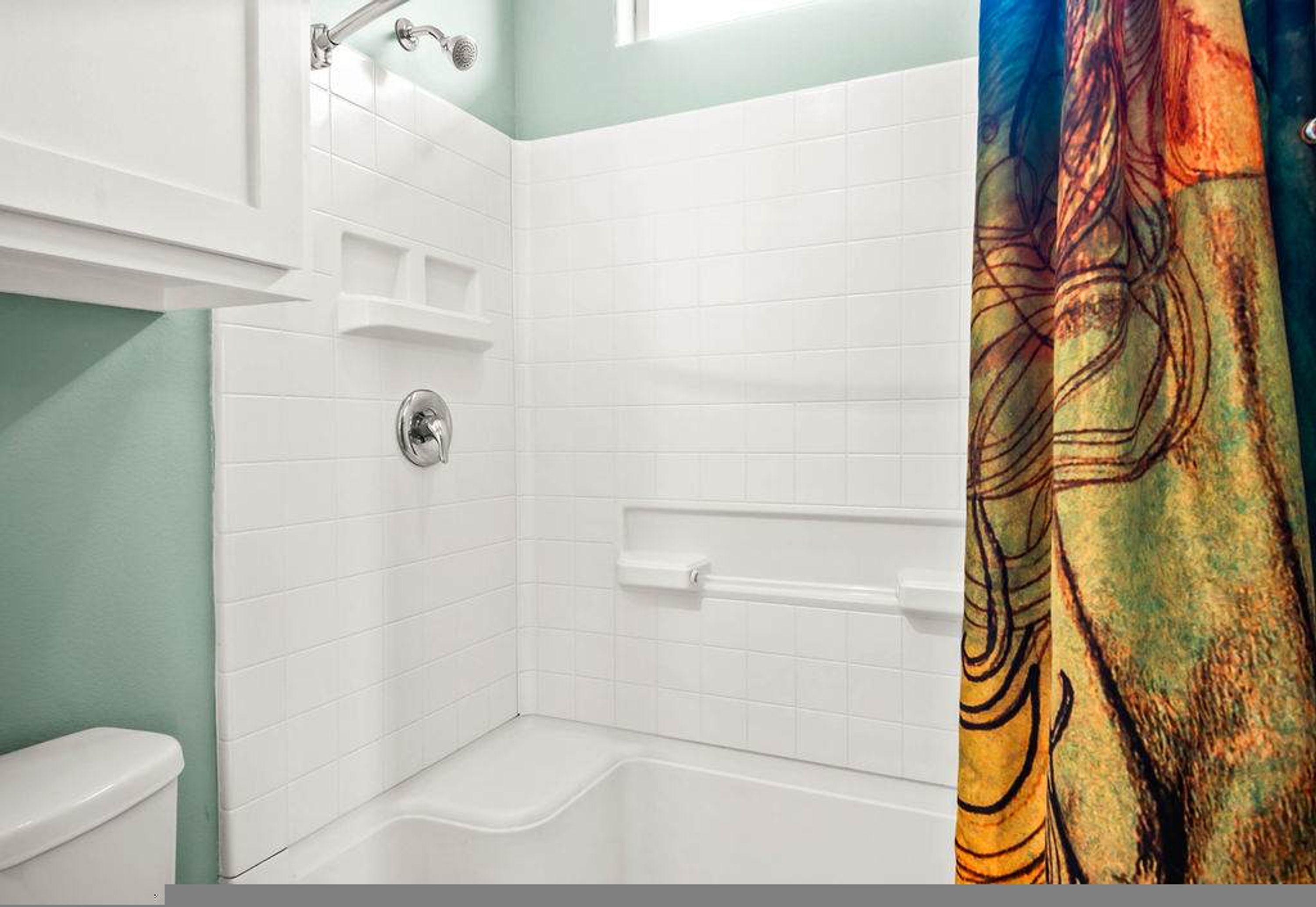 A bathroom with a white tiled shower area, a toilet, and a colorful shower curtain.