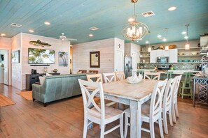Uma sala de estar ampla com mesa e cadeiras de jantar, um sofá e uma cozinha equipada com eletrodomésticos modernos.