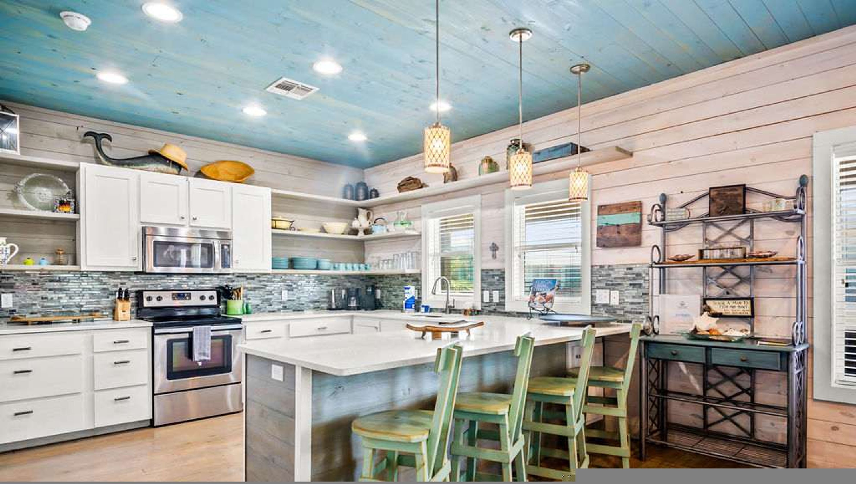 A modern kitchen with white cabinets, stainless steel appliances, a large island with bar stools, and pendant lighting.