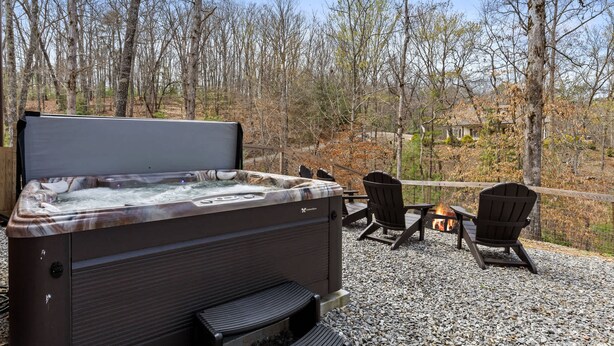 Een hottub met een houten terras, omgeven door bomen en een vuurkuil.
