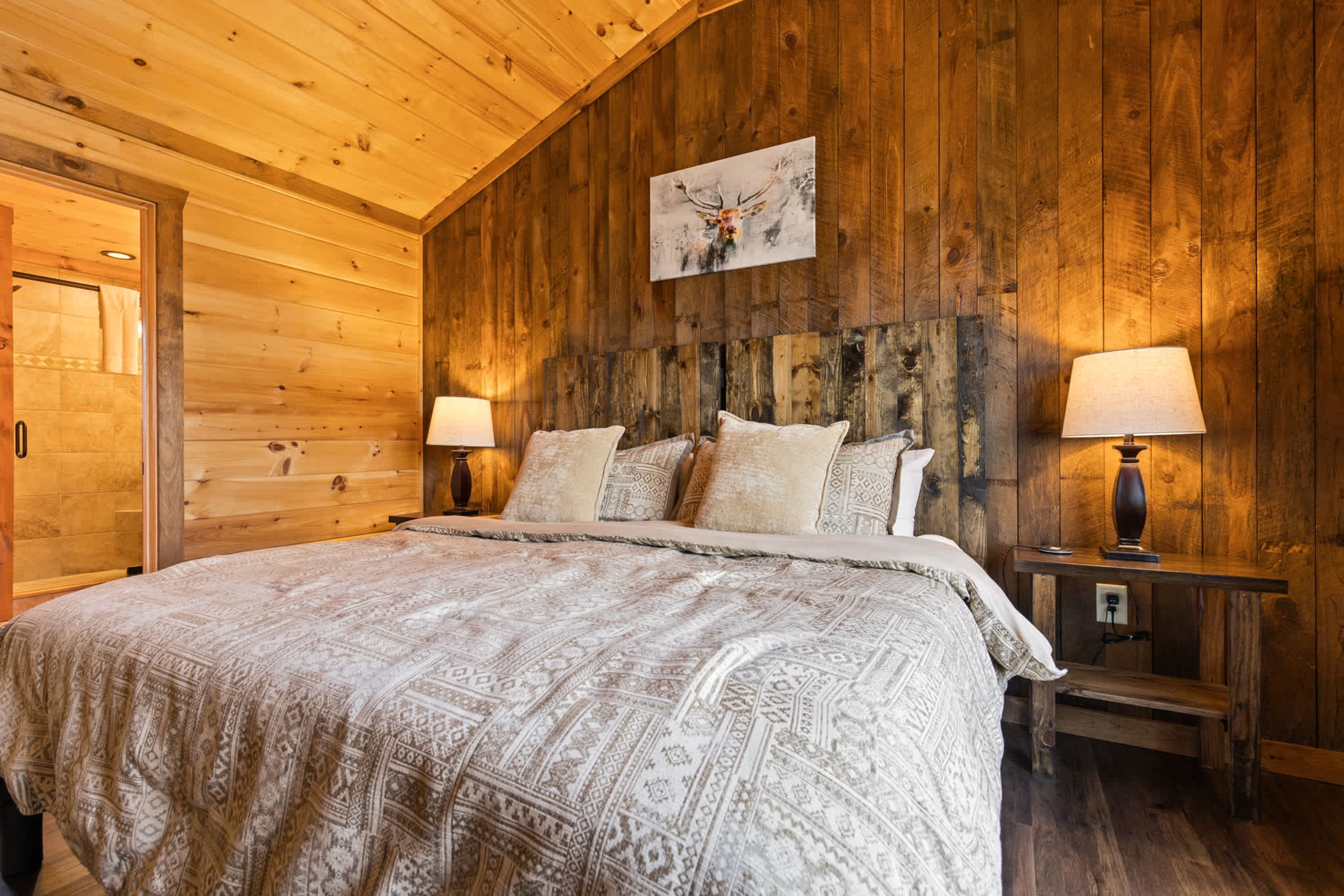 A wooden room with a bed, two bedside lamps, and a wall-mounted picture.